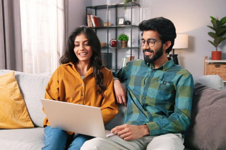 Happy couple resting on sofa in living room searching internet